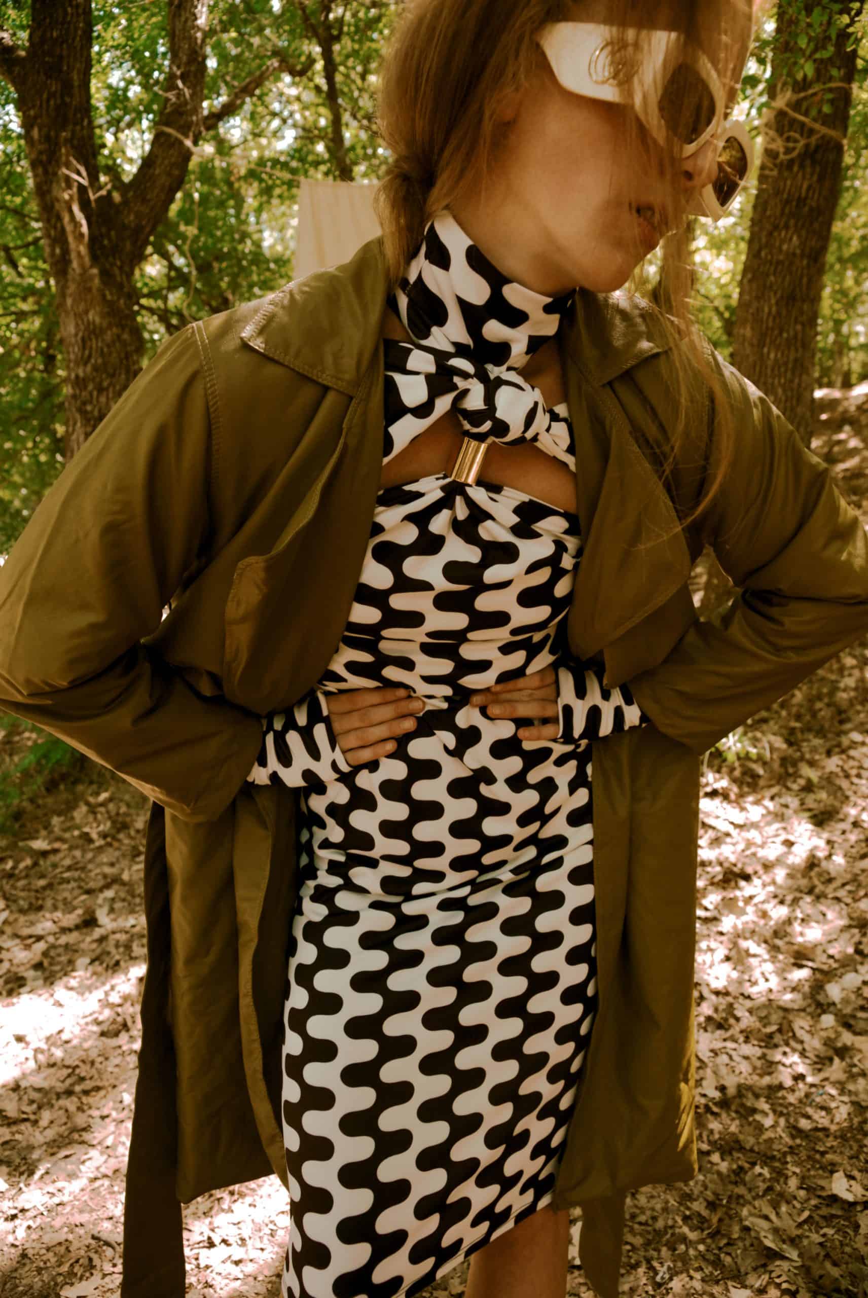 Person wearing a patterned dress and green jacket in a forest setting