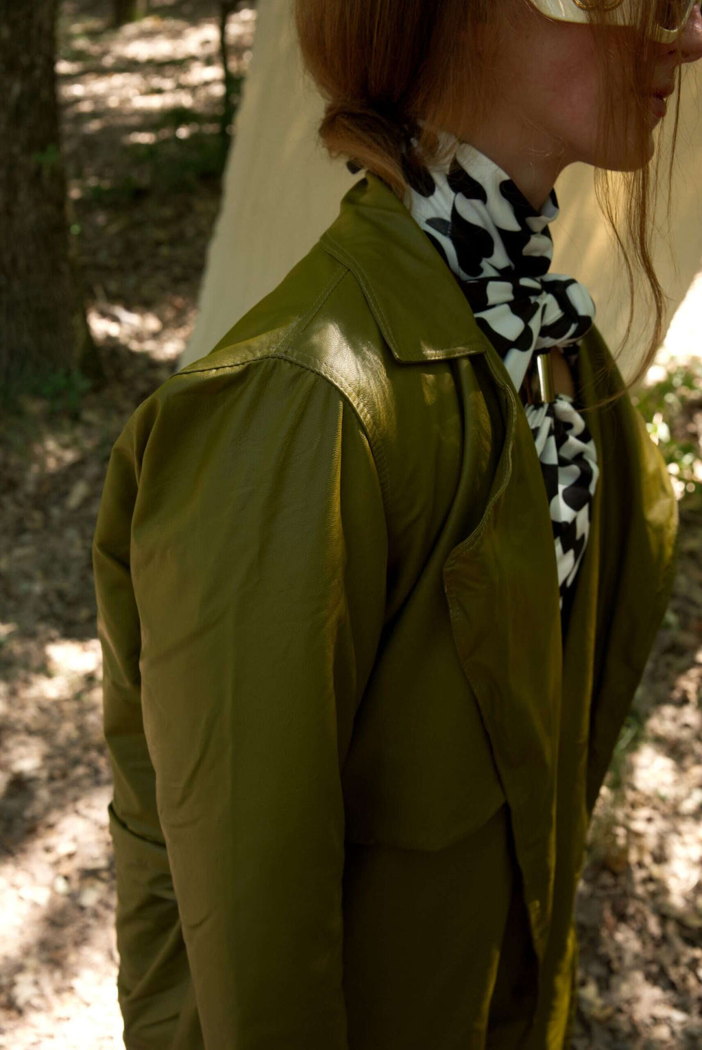 Person wearing a green jacket and a black and white patterned scarf outdoors.