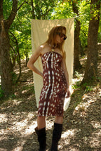 Woman in a patterned dress standing in a forest with a white curtain.