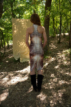 Person wearing a patterned dress standing in a forest with a large yellow card in front of them.