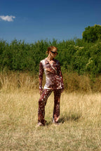 Person wearing a patterned outfit standing in a field with trees in the background
