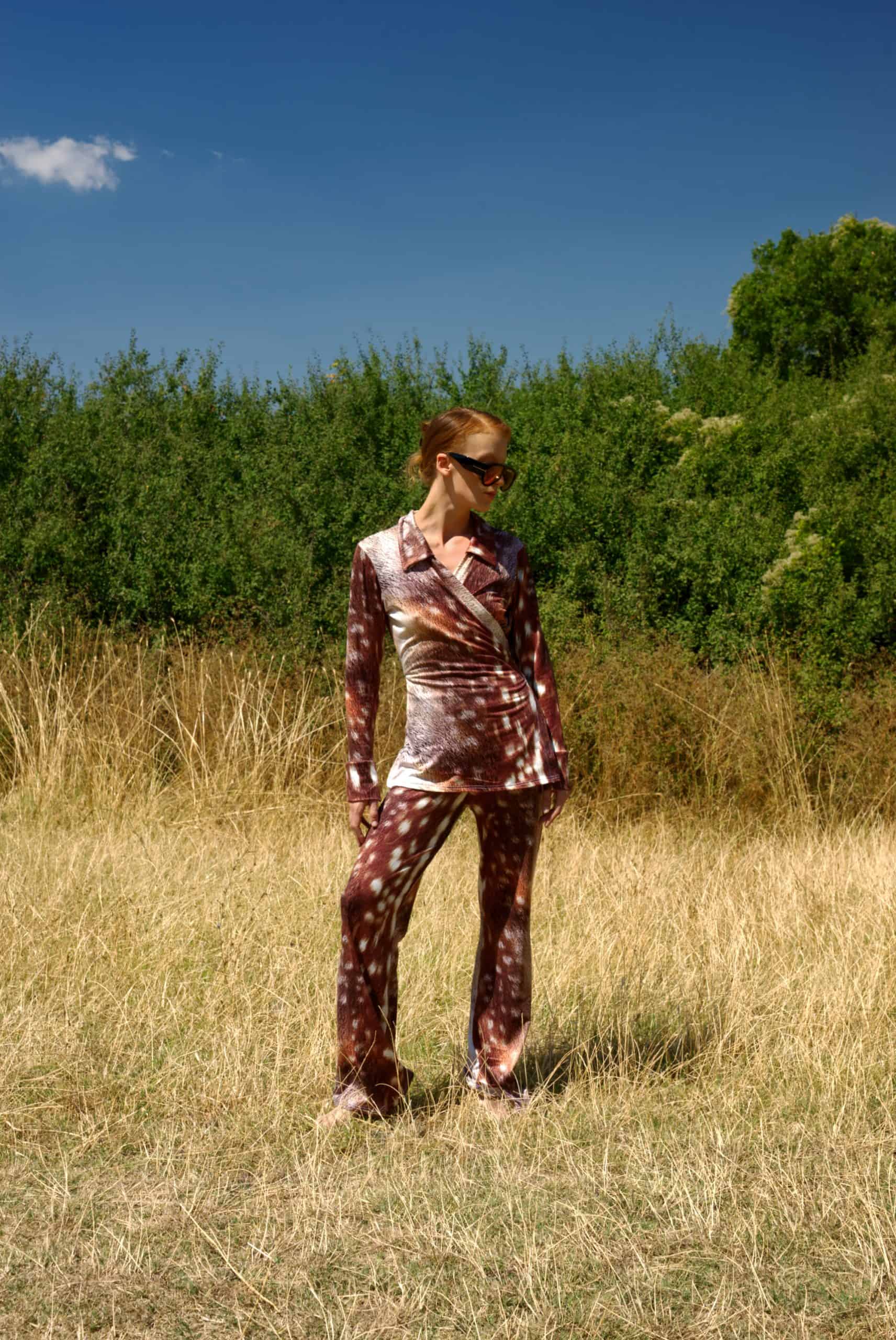 Person wearing a patterned outfit standing in a field with trees in the background