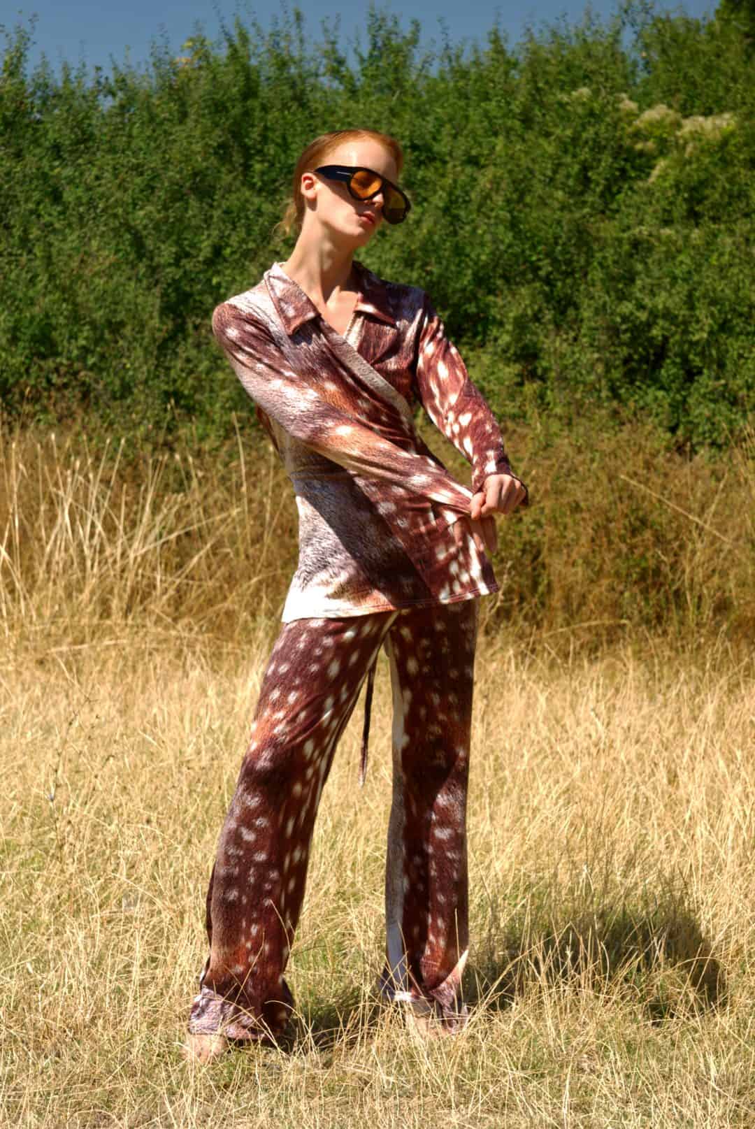 Person wearing a patterned outfit standing in a grassy field with trees in the background