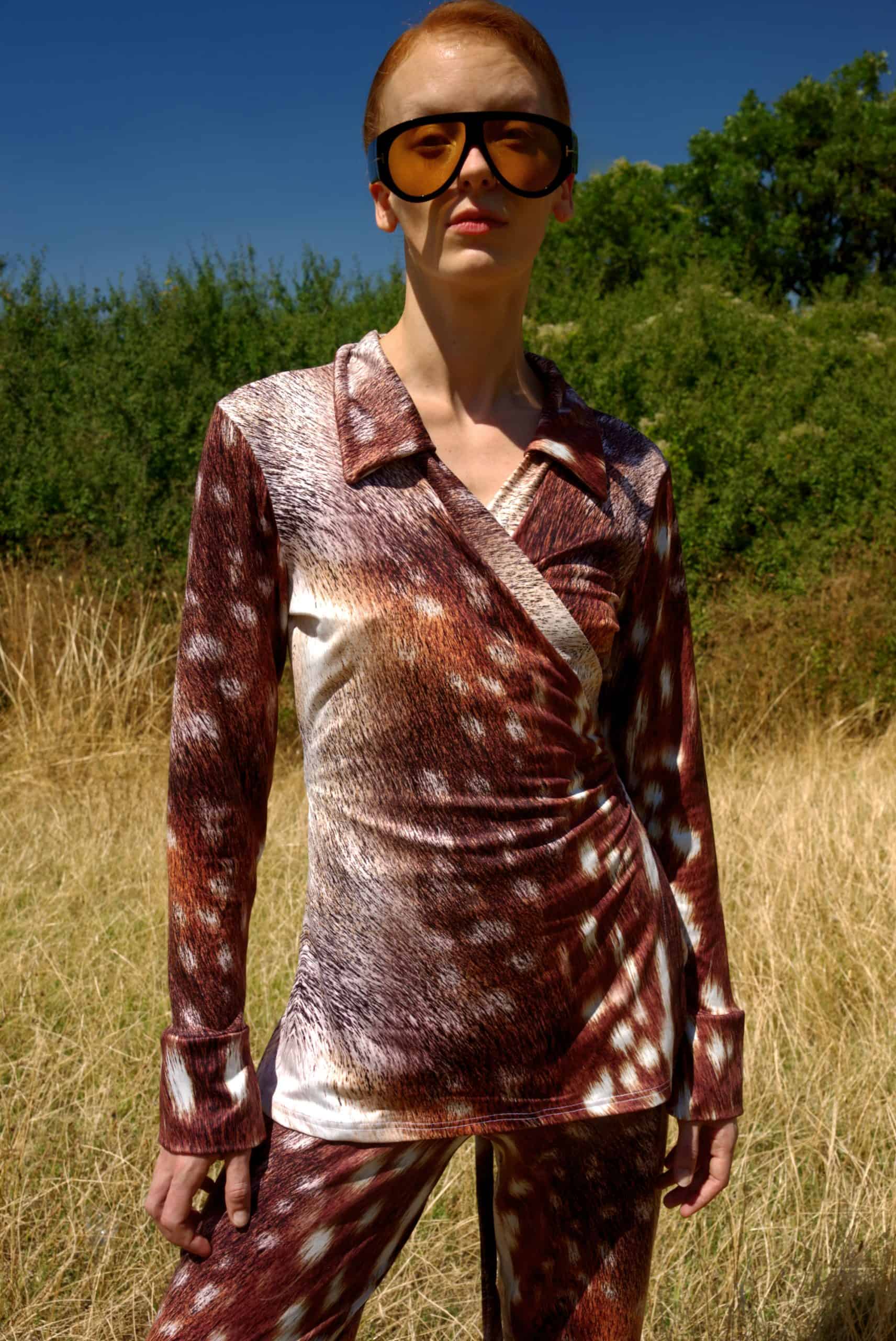 Person wearing a patterned outfit and sunglasses in an outdoor setting with greenery.
