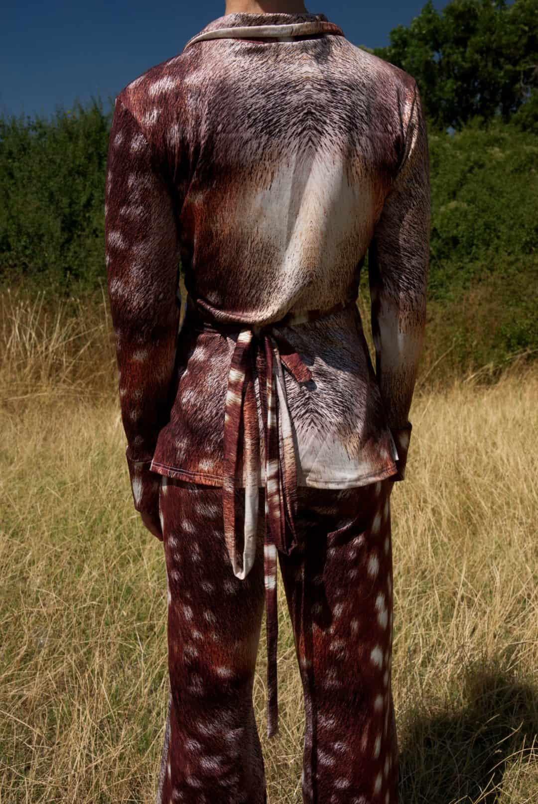 Person wearing a patterned outfit standing in a field with trees in the background