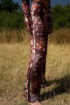 Person wearing a patterned outfit standing in a grassy field with trees in the background