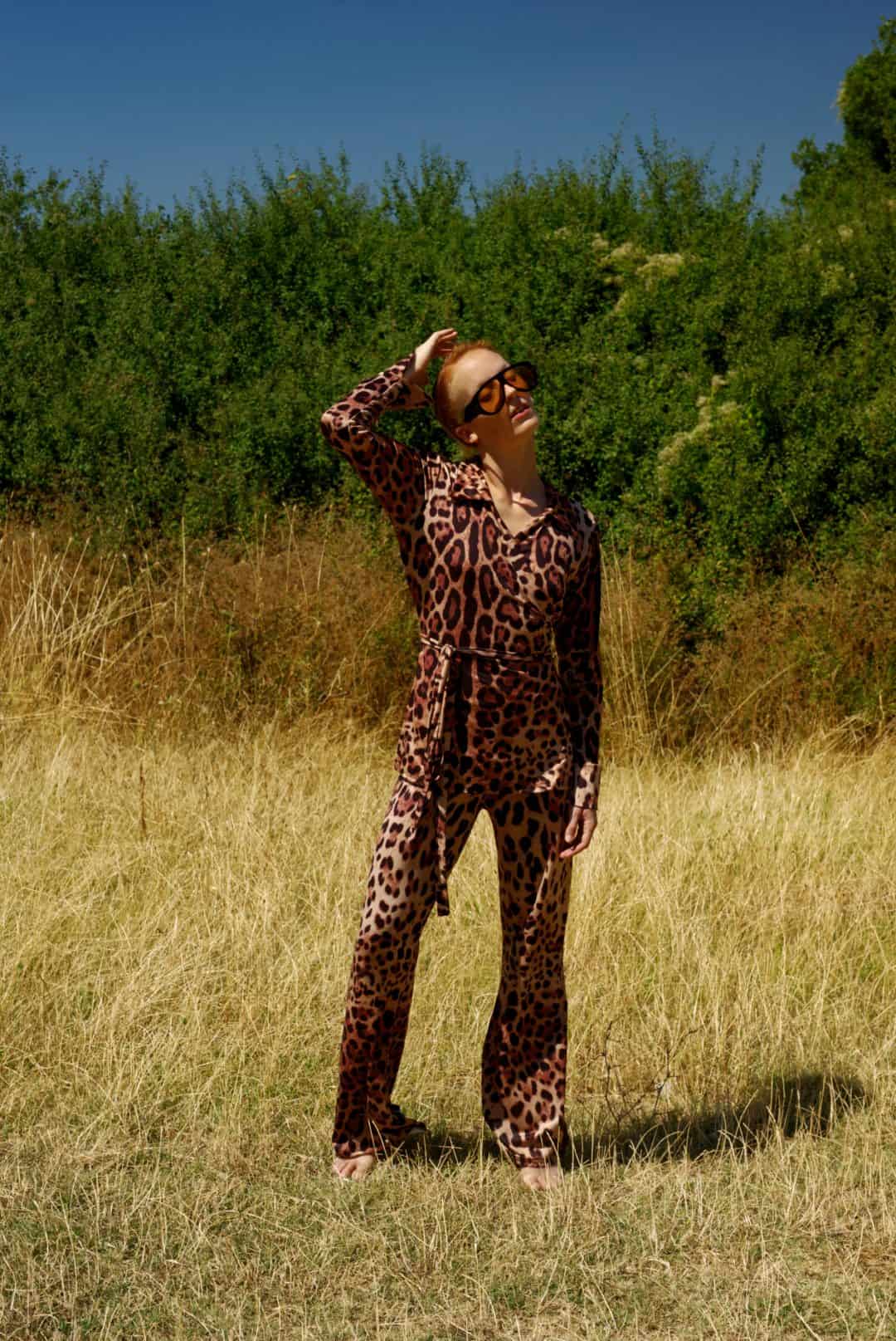 Person wearing a leopard print outfit standing in a grassy field with trees in the background