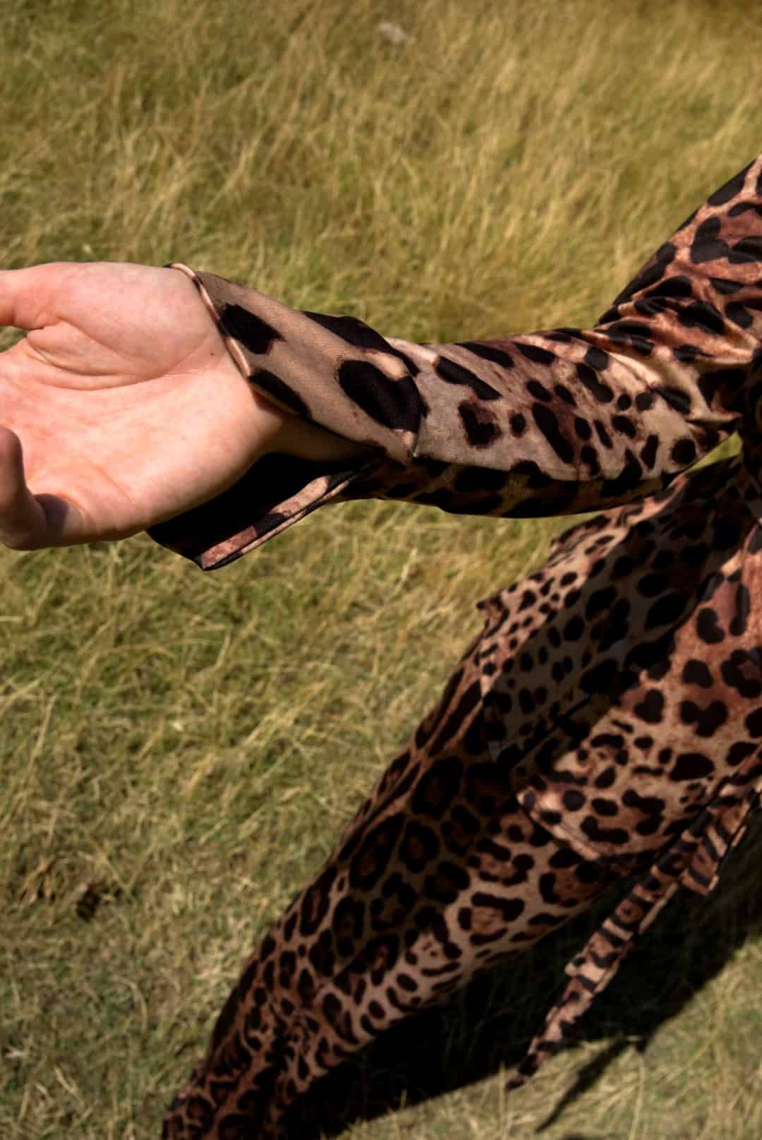 Person wearing a leopard print sleeve against a grassy background