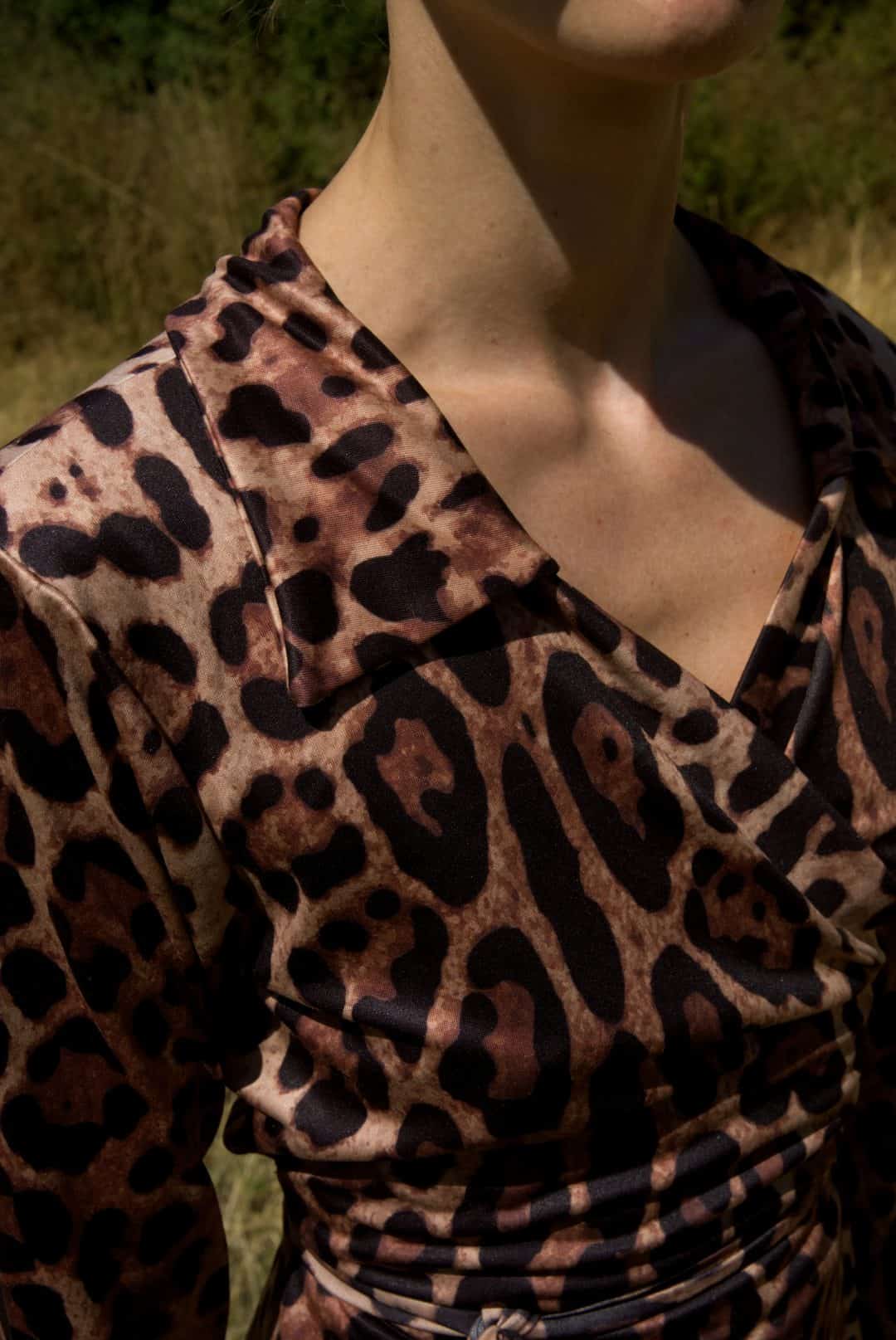 Close-up of a person wearing a leopard print top with a blurred natural background