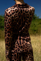 Person wearing a leopard print outfit standing in a grassy field with trees in the background.