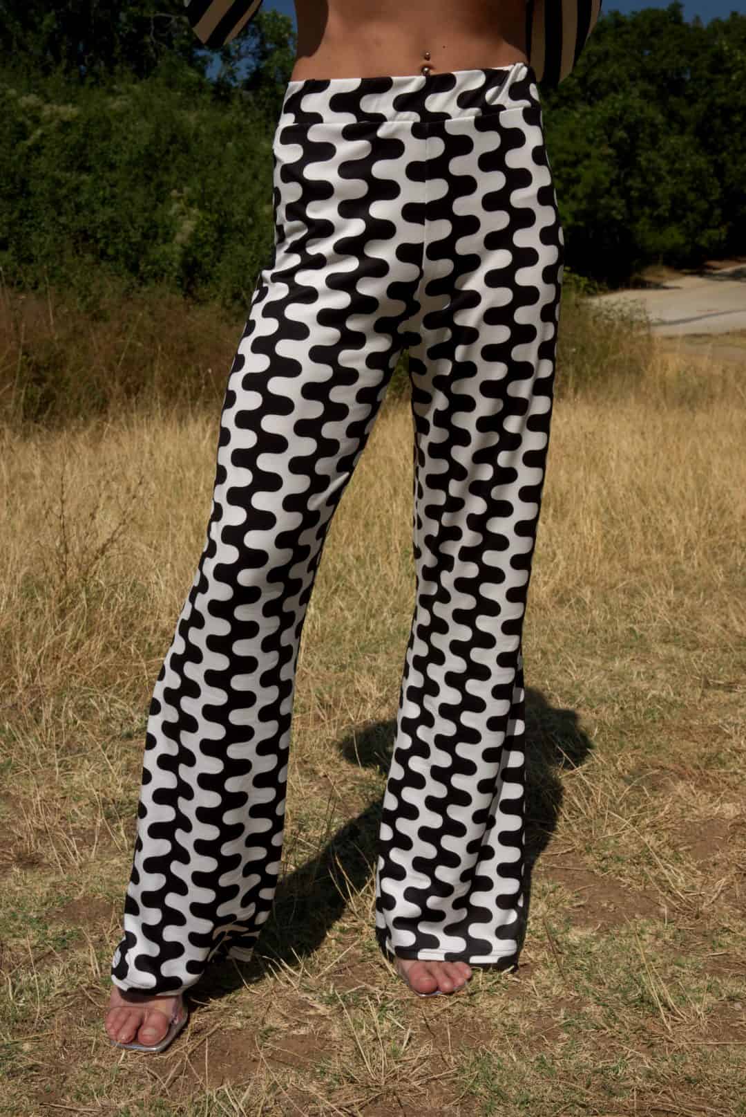 Person wearing black and white patterned pants standing in a grassy outdoor area.