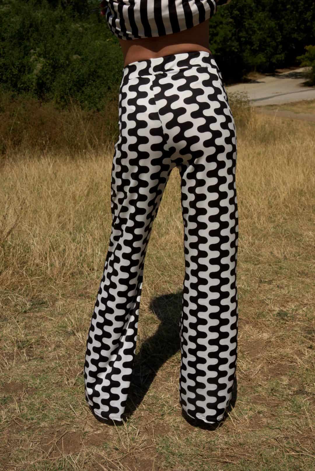 Person wearing black and white patterned pants standing in a grassy field.