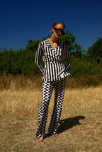 Person wearing a black and white checkered outfit standing in a field with trees in the background