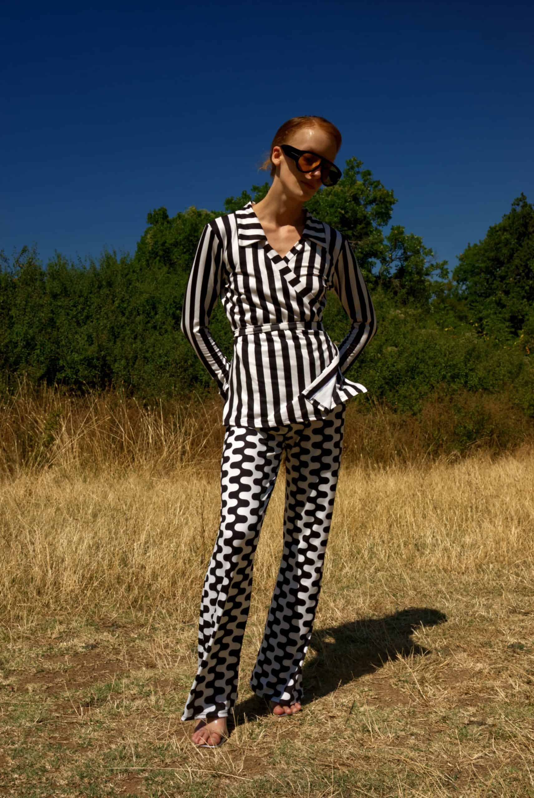 Person wearing a black and white checkered outfit standing in a field with trees in the background