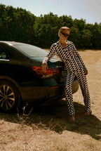 Person in a checkered outfit standing next to a car in an outdoor setting