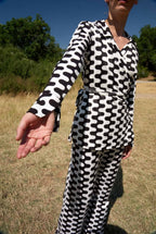 Person wearing a black and white patterned outfit standing in an outdoor setting with trees and grass.
