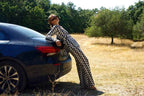Person in checkered outfit leaning against a car in a natural setting