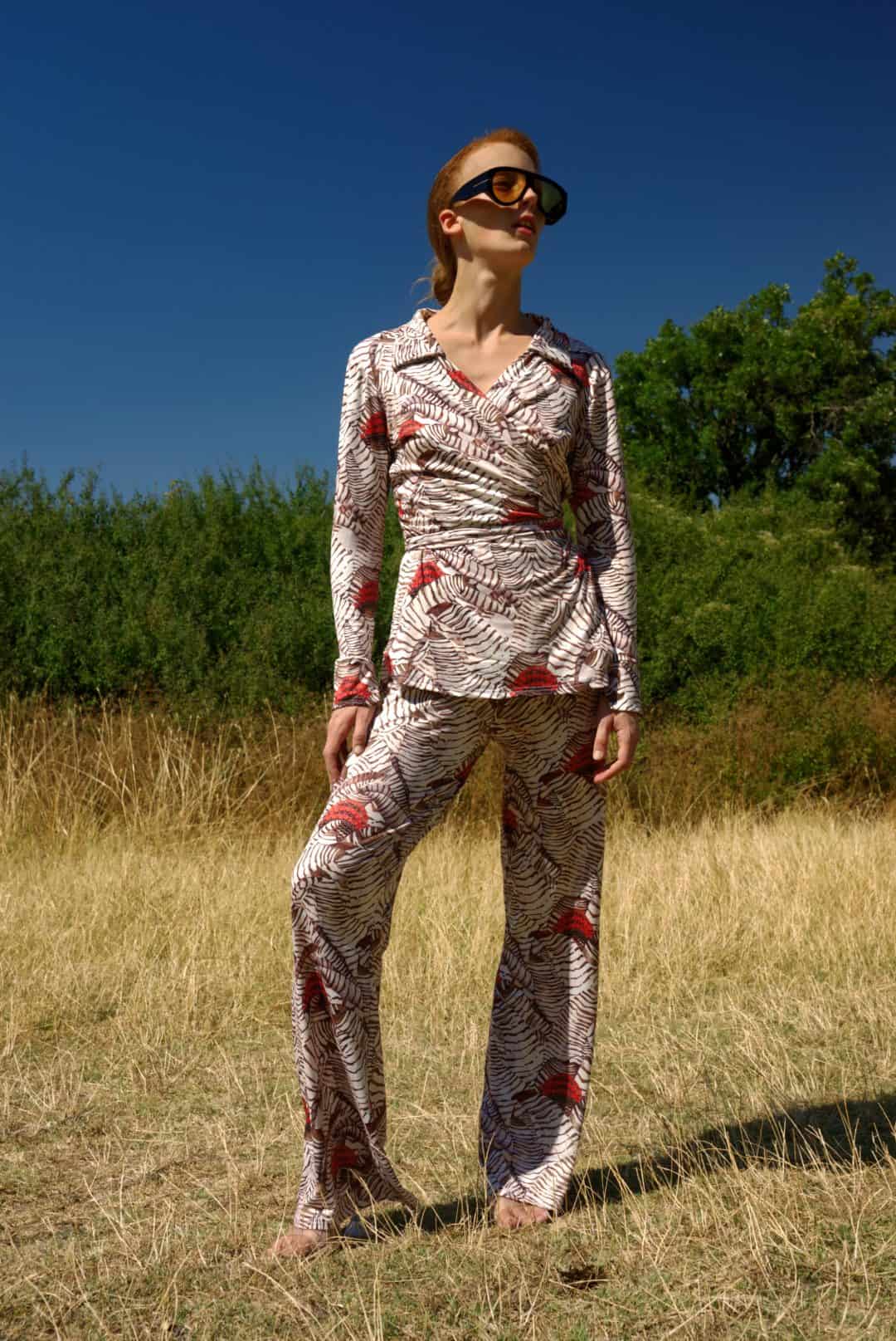 Woman in a patterned outfit standing in a field with a clear blue sky.