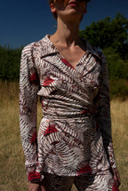 Person wearing a patterned outfit standing in a natural setting with trees and grass.
