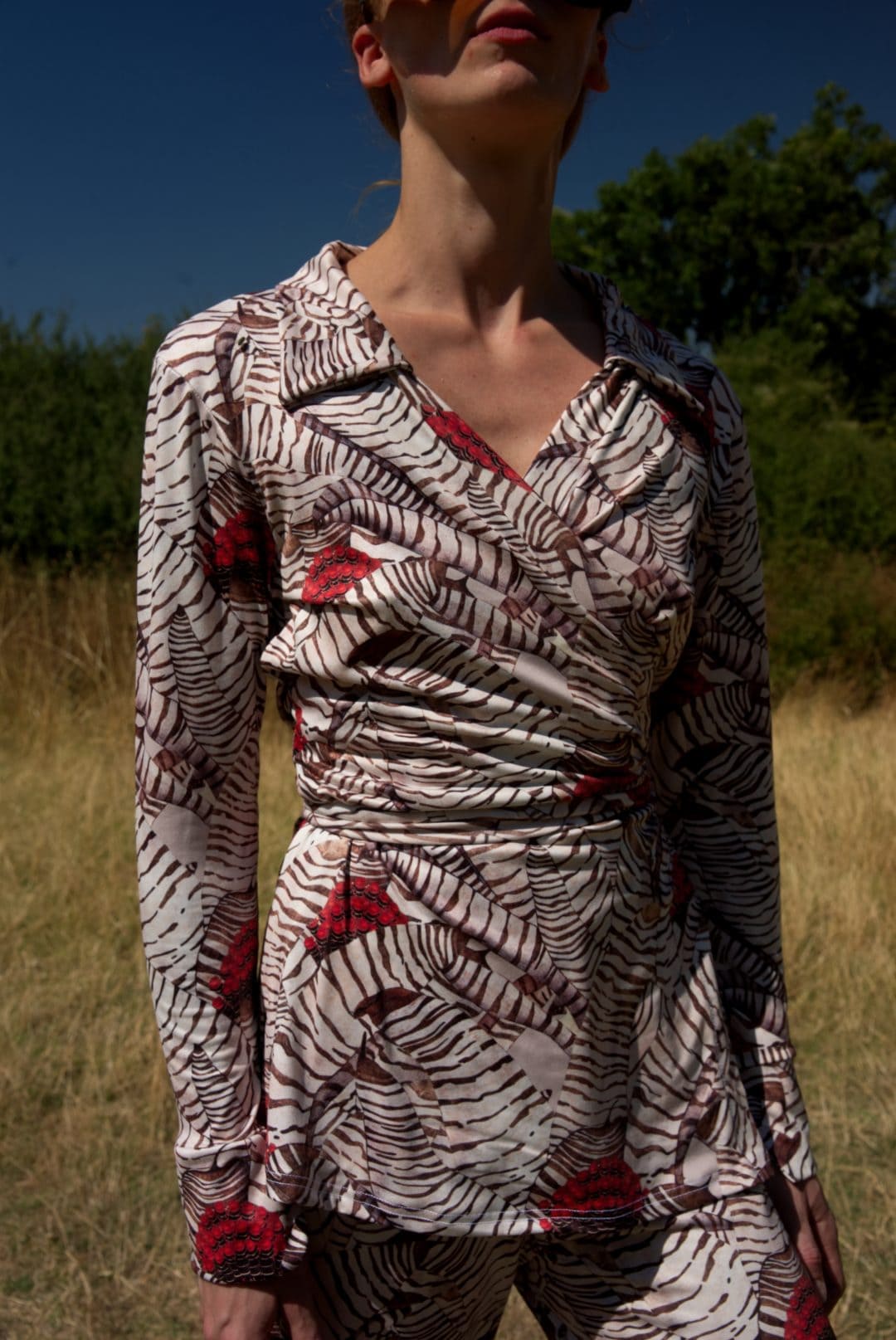 Person wearing a patterned outfit standing in a natural setting with trees and grass.