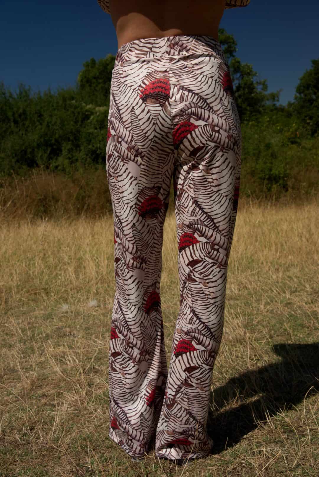 Person wearing patterned pants standing in a field with trees in the background