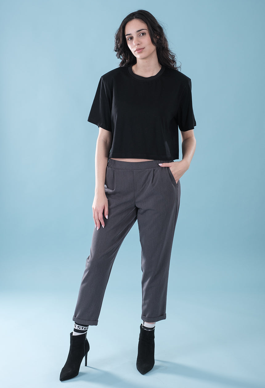 Woman wearing a black crop top and gray pants on a light blue background