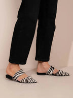 Person wearing black and white zebra-striped sandals with black pants on a beige background