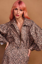 A model wearing a brown animal print zip jacket and standing against a plain background.