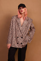 A person wearing a leopard print oversized blazer with black buttons, paired with black pants and a black cap.