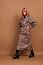 A model wearing a brown animal print zip jacket and standing against a plain background.