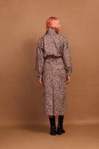 A model wearing a brown animal print zip jacket and standing against a plain background.