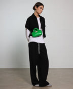 Person wearing a black jacket, white shirt, and black pants with a green bag on a plain background