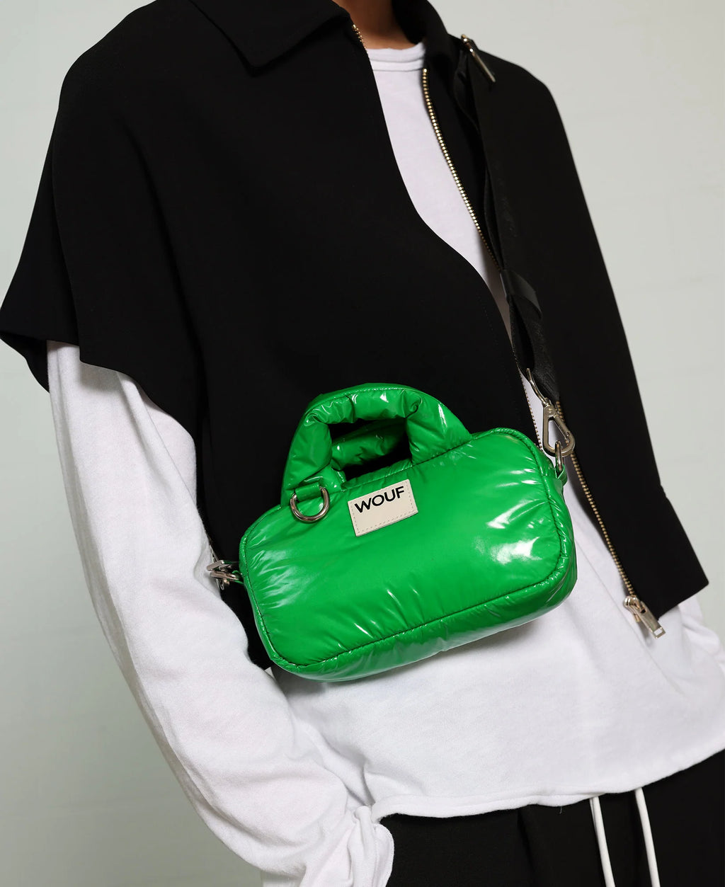 Green puffer handbag with 'Wouf' brand logo worn by a person in black and white outfit.