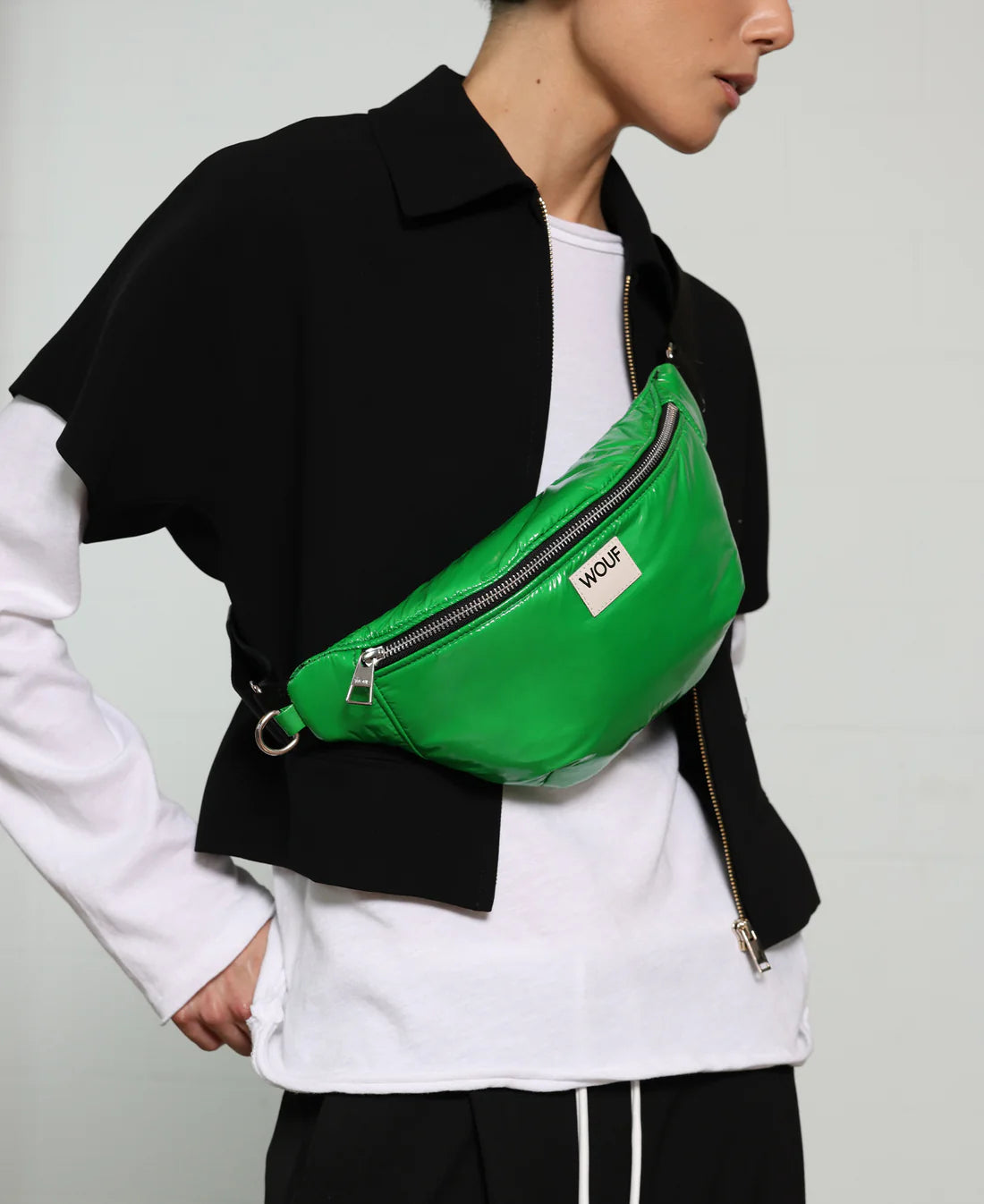 Person wearing a green waist bag with a visible brand logo on a plain background