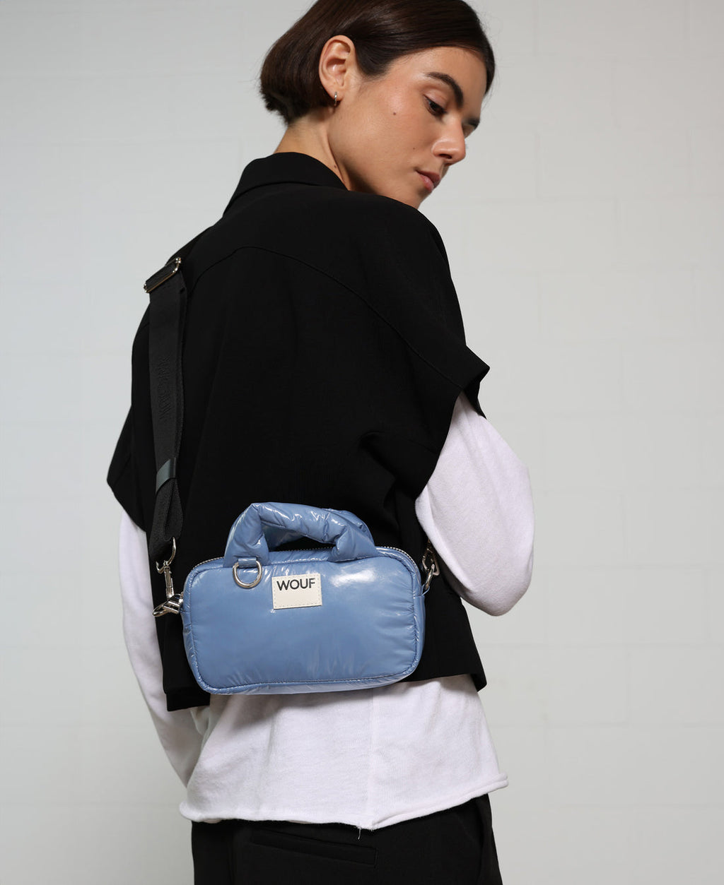 Person wearing a black jacket with a blue handbag on a plain background