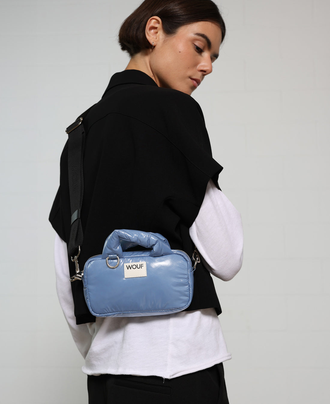Person wearing a black jacket with a blue handbag on a plain background
