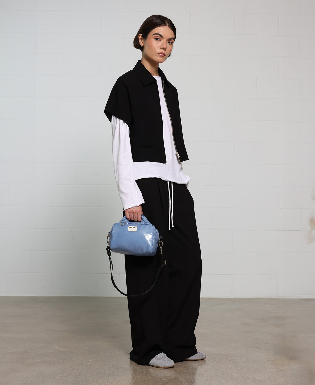 Person wearing a black and white outfit with a blue handbag against a plain background