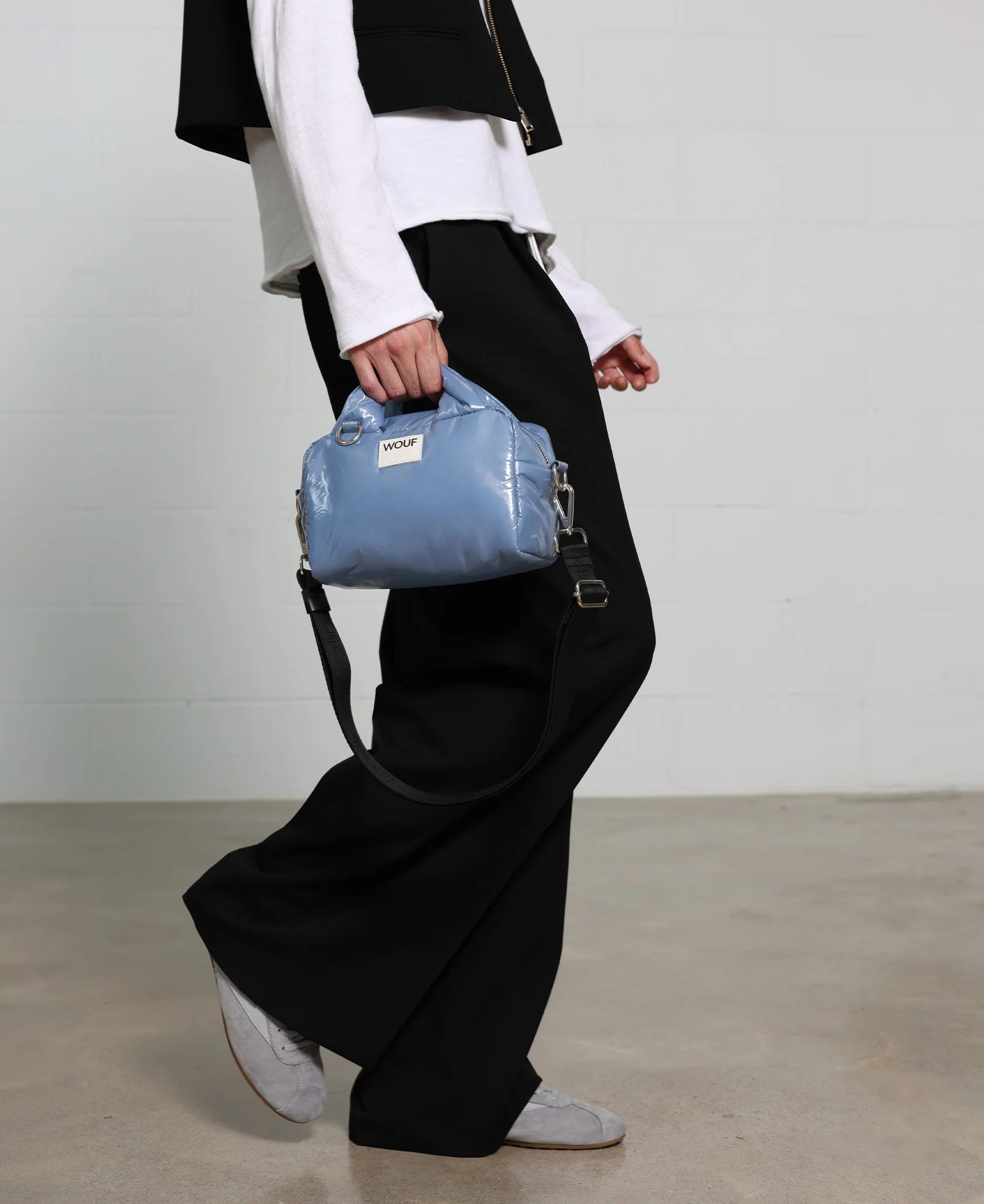 Person holding a blue handbag with a visible brand logo against a plain background