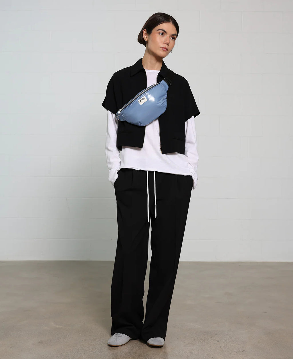 Person wearing a black and white outfit with a blue fanny pack against a plain background