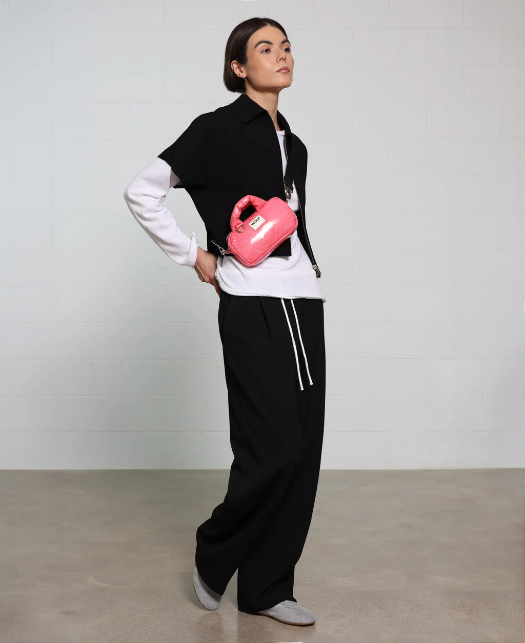 Person wearing a black vest, white shirt, and black pants holding a pink object against a plain background