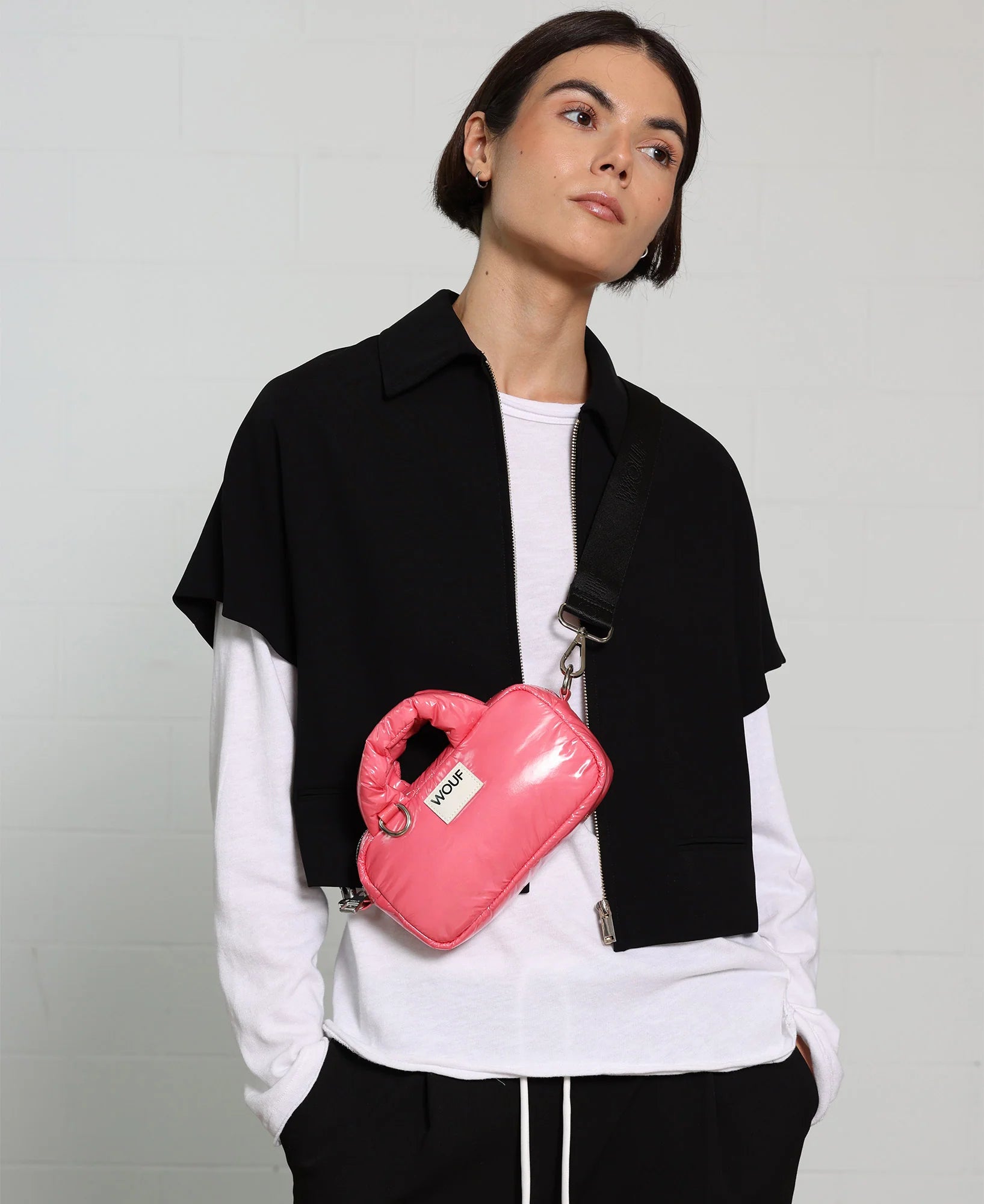 Person wearing a black jacket and white shirt with a pink bag on a gray background
