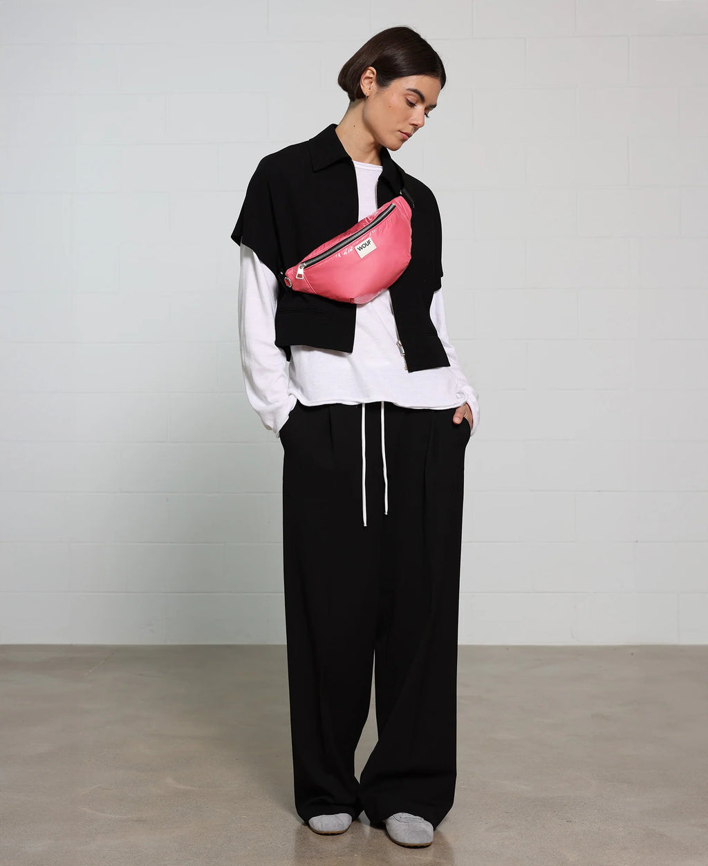 Person wearing a black and white outfit with a pink fanny pack on a plain background