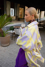 Woman in a yellow and purple outfit walking outdoors in a modern setting.