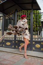 Woman in patterned shirt dress, beret, and high heels walking in front of a black and gold fence.