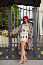 A woman in a red beret, leopard print coat, geometric print dress, and patterned heels stands in front of a black and gold gate.