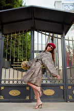A woman poses in a leopard print coat and matching heels, wearing a red beret and sunglasses in front of a black and gold gate.
