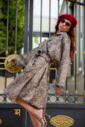 A woman in a leopard-print dress, red beret, and sunglasses leans against a gate.