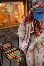 Person sitting outside a Starbucks store wearing a patterned coat and blue cap.