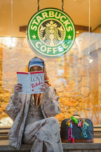 Person reading a book in front of a Starbucks coffee shop window