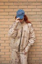 Person wearing a beige tracksuit with celestial patterns against a brick wall.
